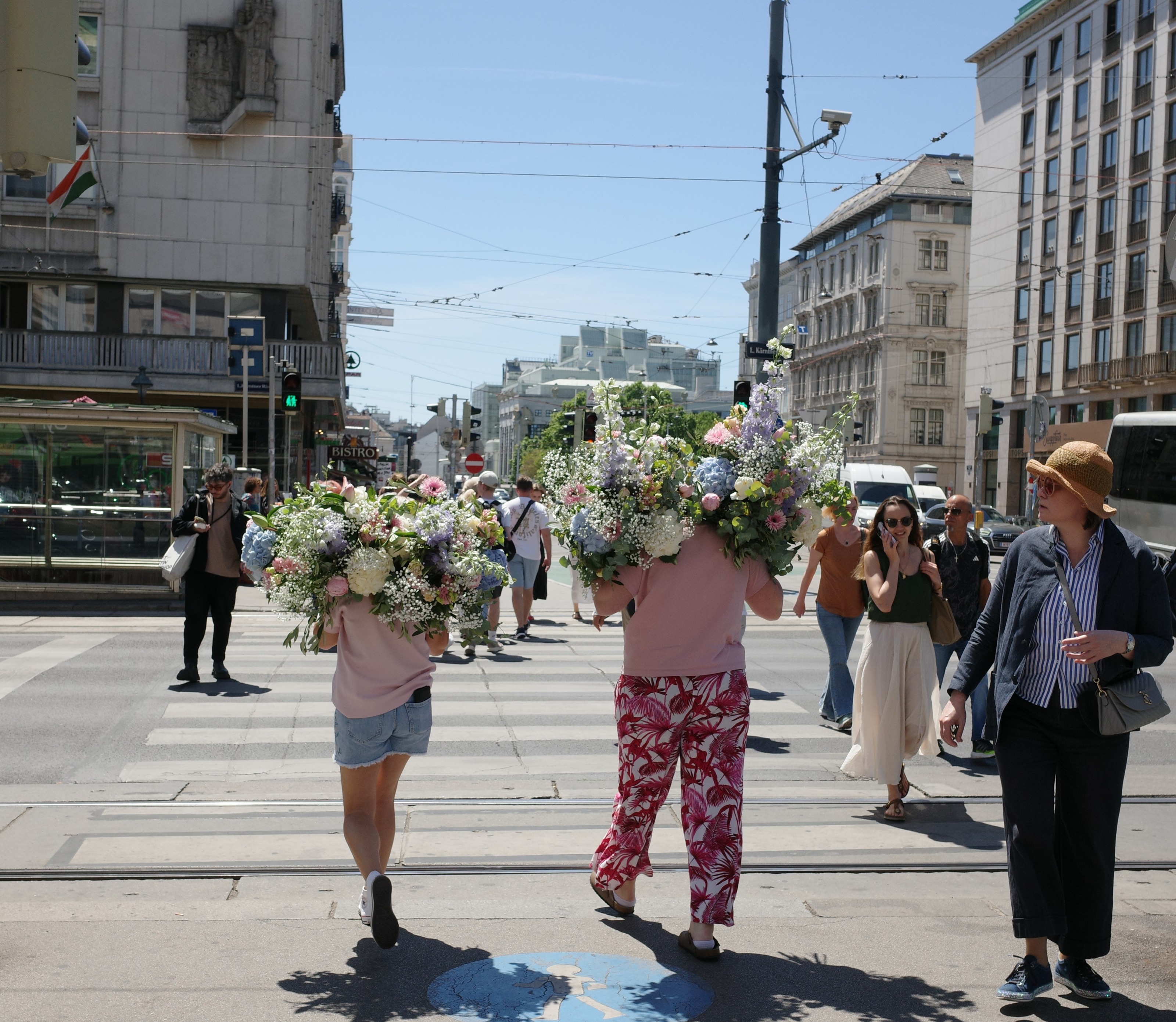 Two people carrying huge flower bouquets across a crossing