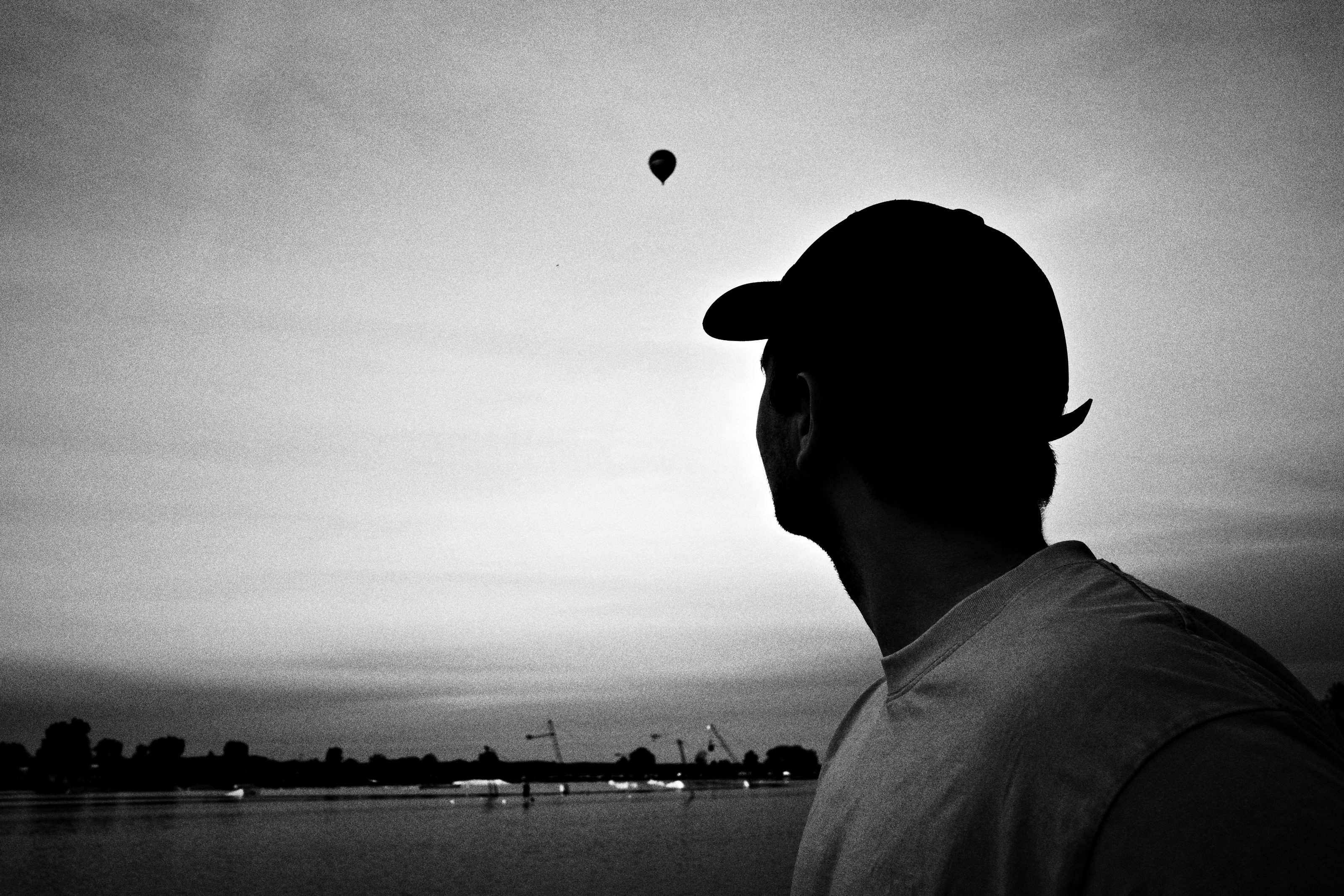 Silhouette of a man in a cap watching a hot-air balloon over a lake