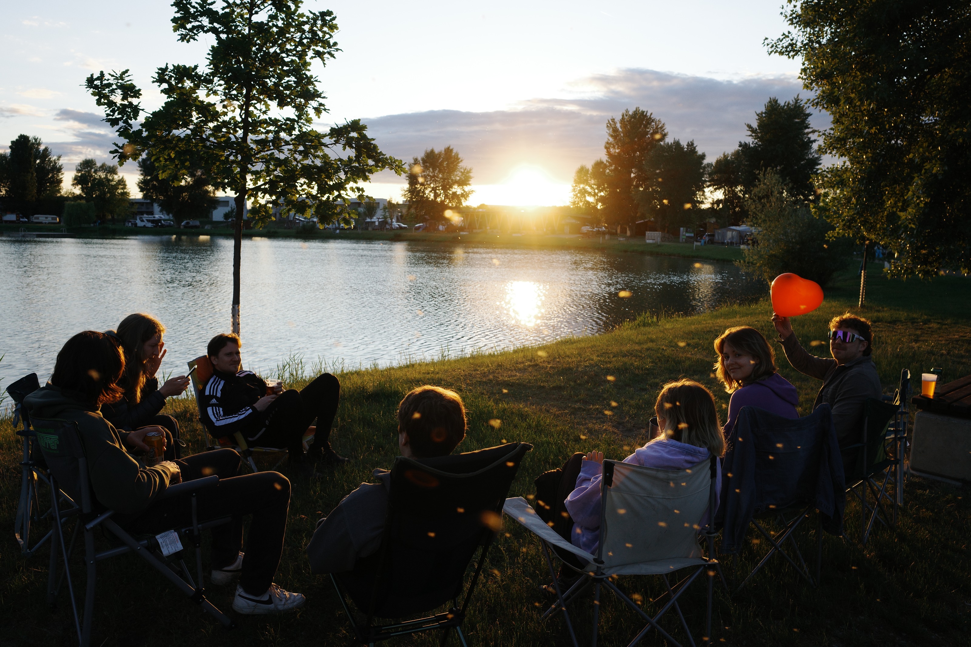 Friends in camping chairs by a lake at sunset