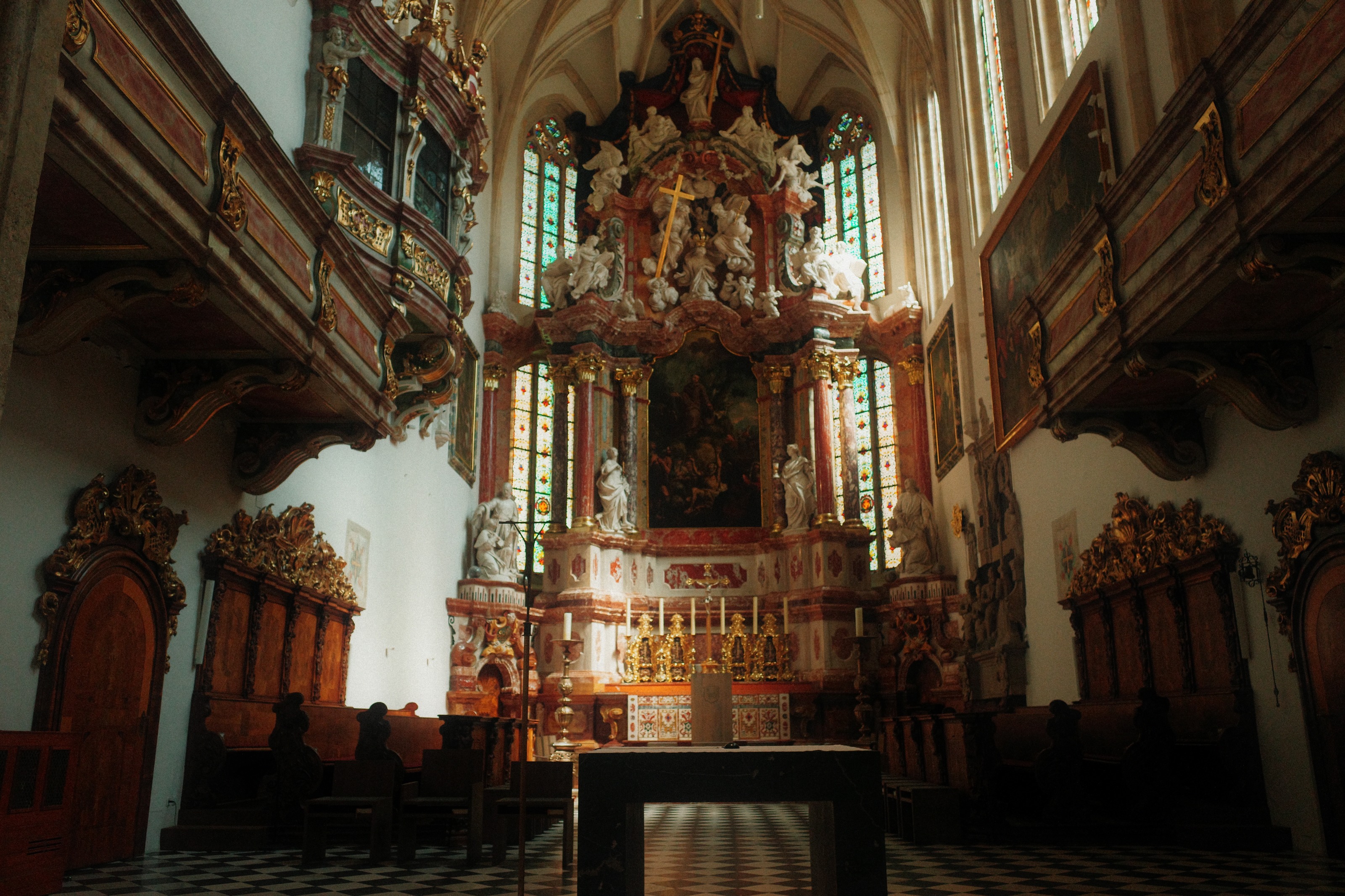 Church nave with a white and gold high altar, stained glass behind it and candles on the table in front