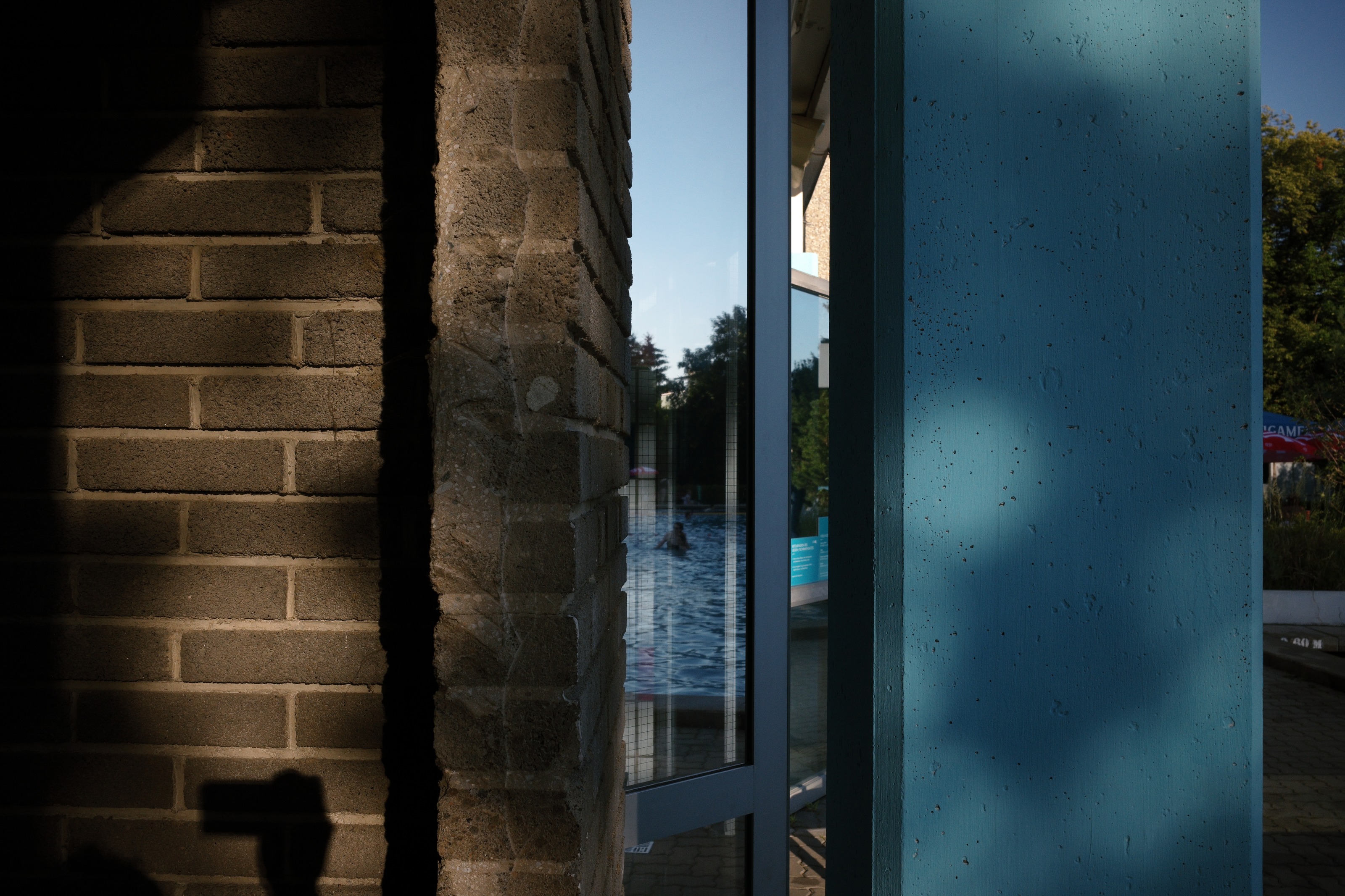 A brick wall in deep shade, the pool visible as a sliver of blue through a glass door